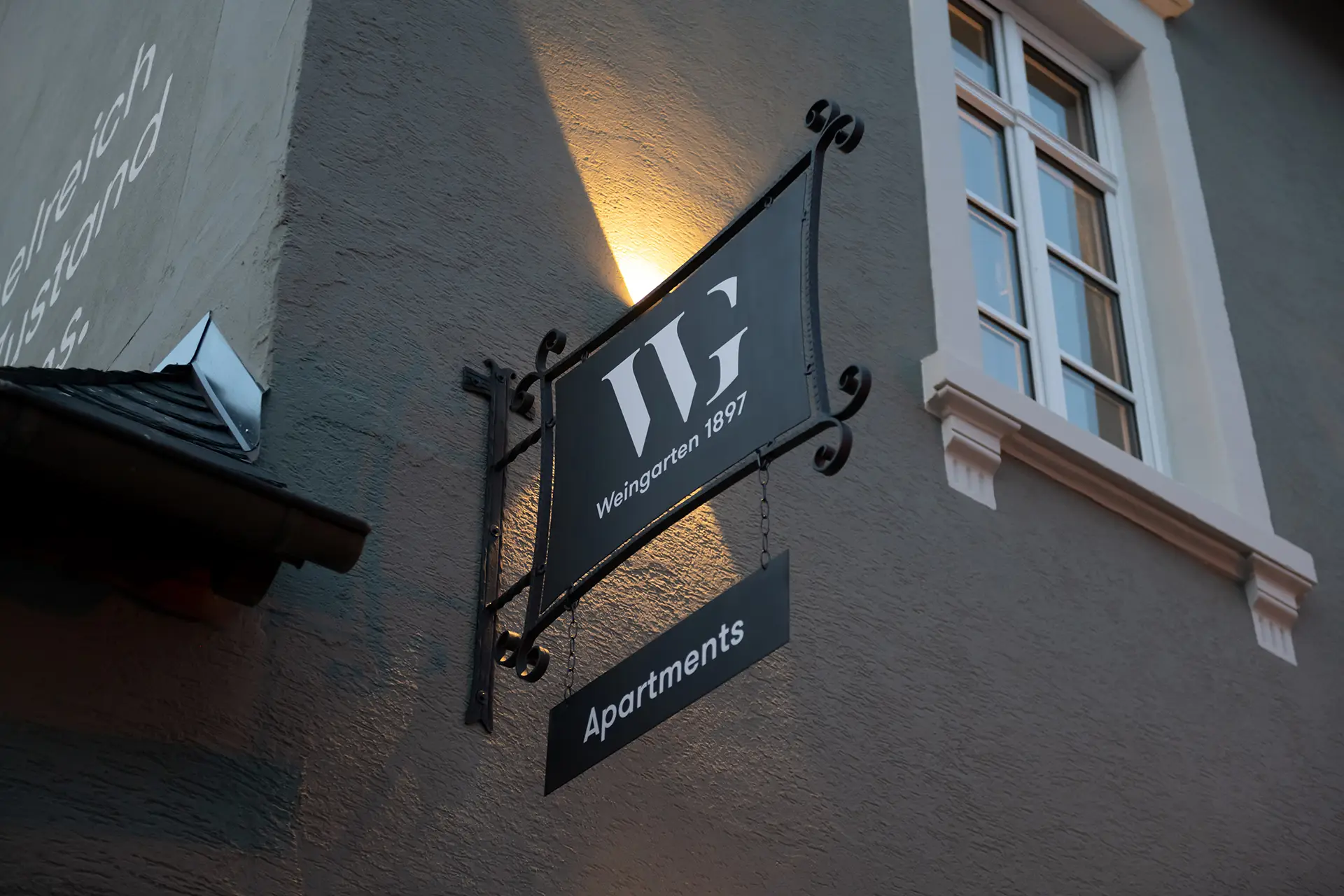 Schmiedeeisernes Schild Weingarten 1897 Apartments im Abendlicht an einer stilvoll renovierten Fassade mit Fenster.